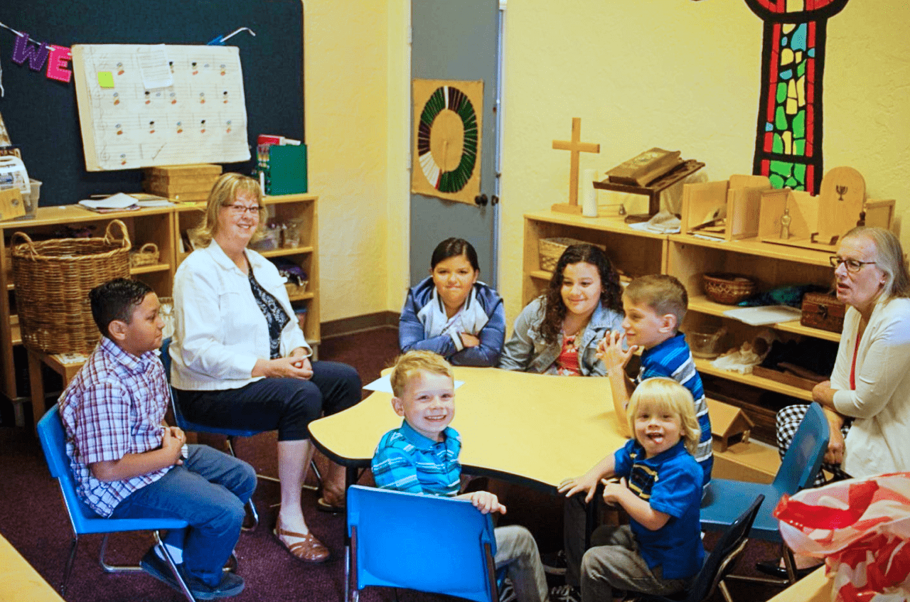 Children and teachers sitting at table inside Sunday school classroom